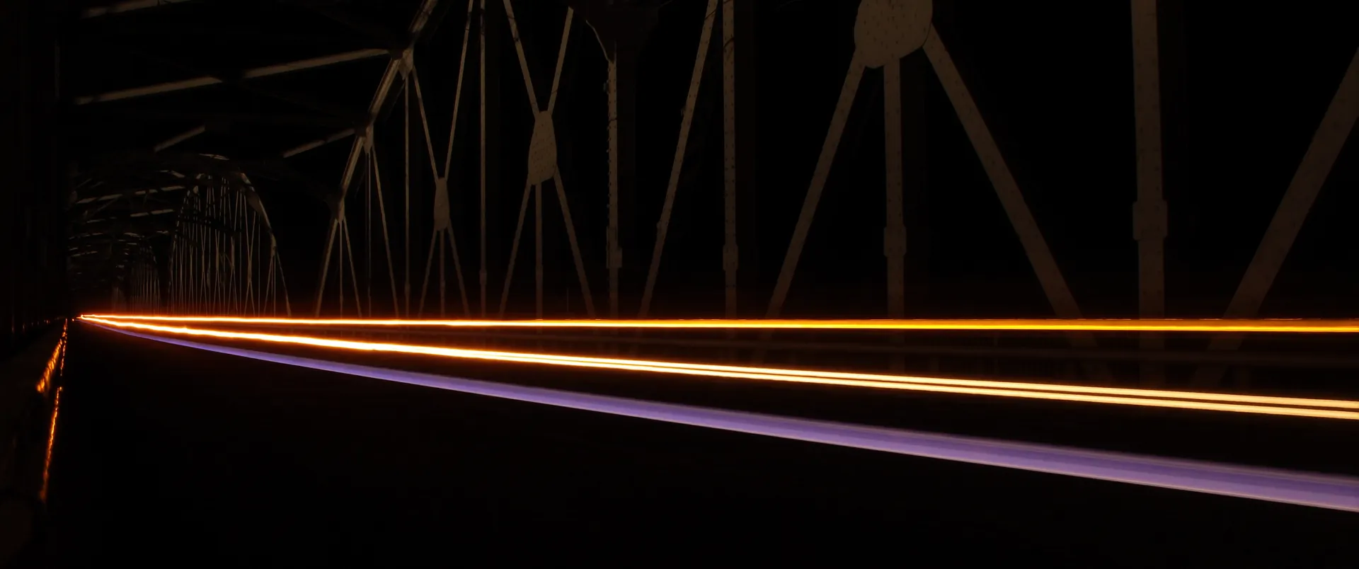 A steel bridge at night with a warm light trail crossing it